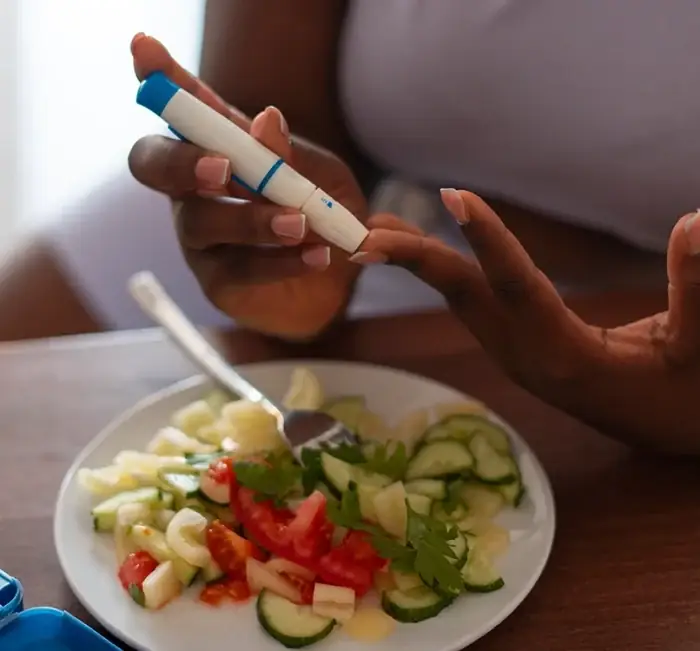 A person using a finger-prick lancet beside a plate of salad