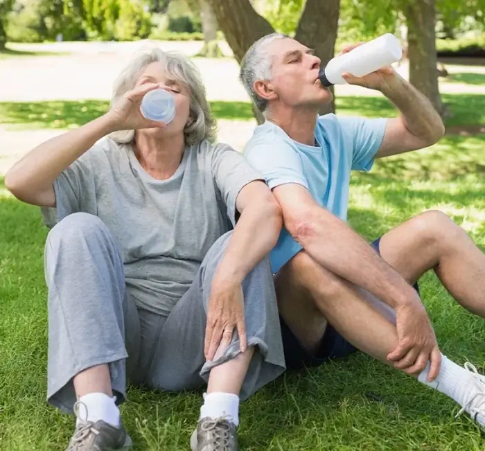 An older couple drinking water sitting on grass in a park